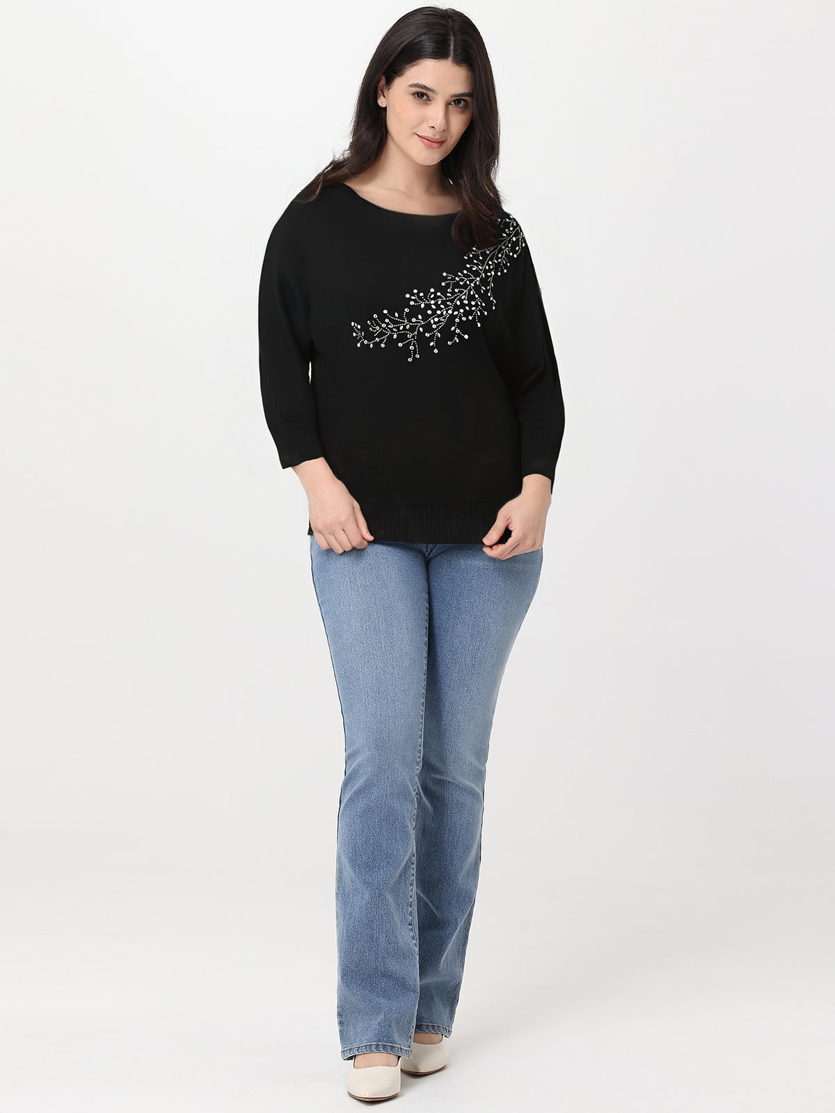 Woman wearing a black sweater with a decorative pattern and blue jeans on a white background
