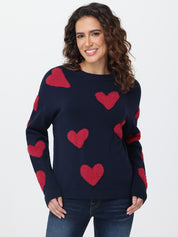 Woman wearing a navy sweater with red heart patterns on a plain background