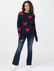 Woman wearing a navy sweater with red heart patterns and blue jeans on a white background