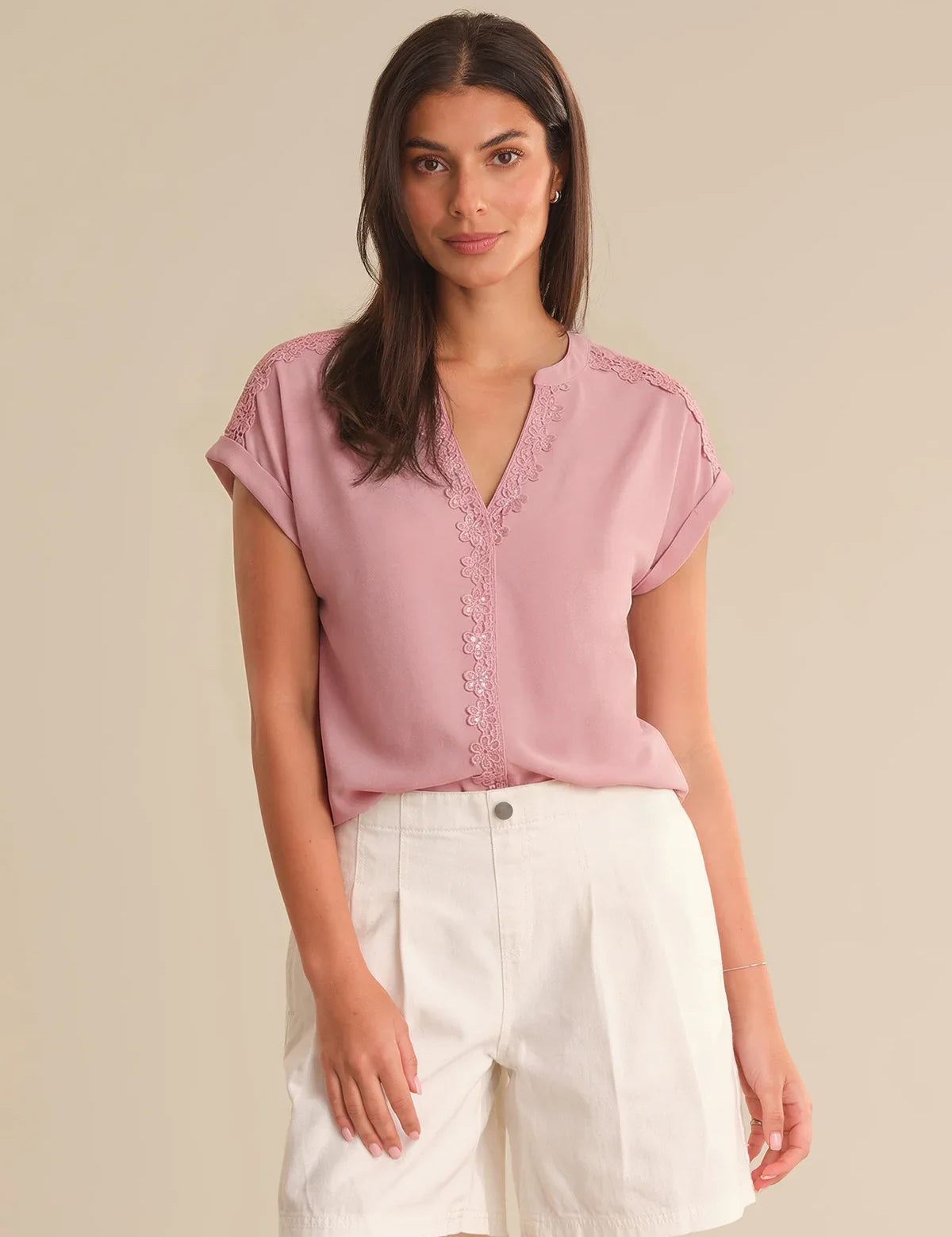 Woman wearing a pink blouse with lace details and white shorts on a beige background
