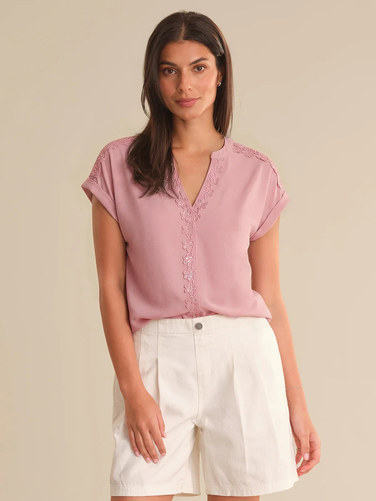 Woman wearing a pink blouse with lace details and white shorts on a beige background