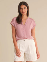 Woman wearing a pink blouse with lace details and white shorts on a beige background