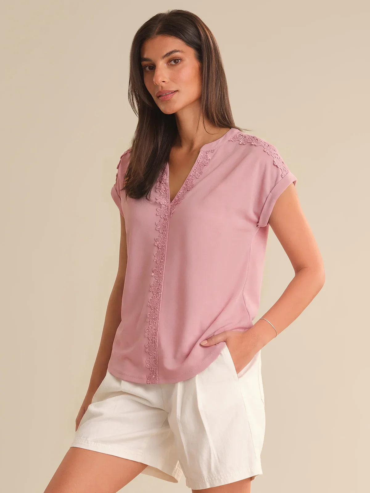 Woman wearing a pink blouse with lace details on a beige background