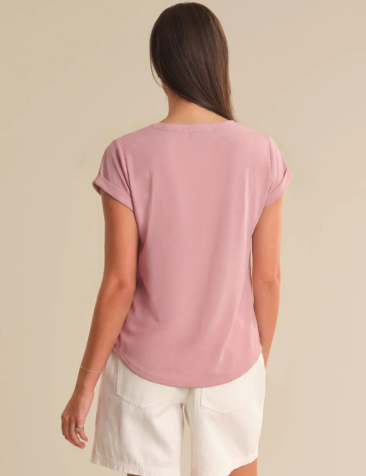 Woman wearing a pink t-shirt and white shorts on a beige background