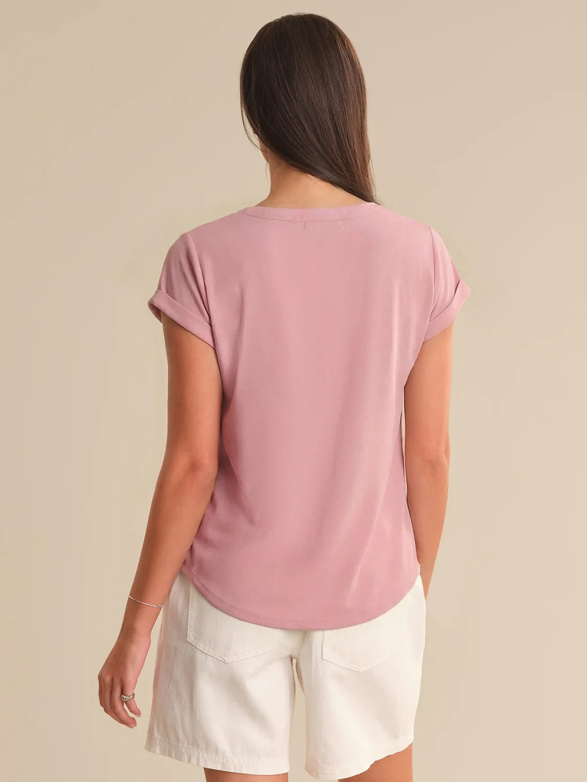 Woman wearing a pink t-shirt and white shorts on a beige background