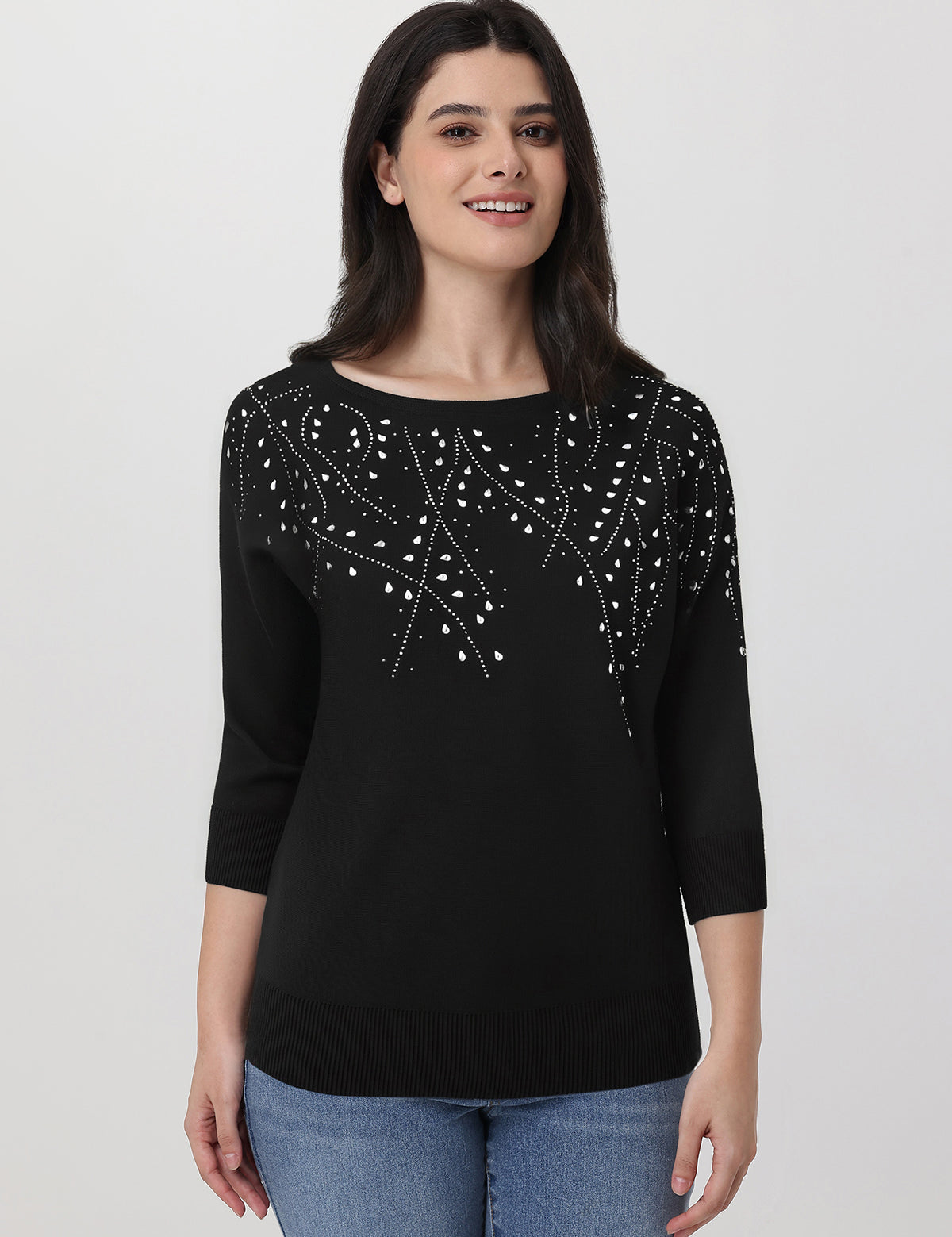 Woman wearing a black sweater with white embellishments on a plain background