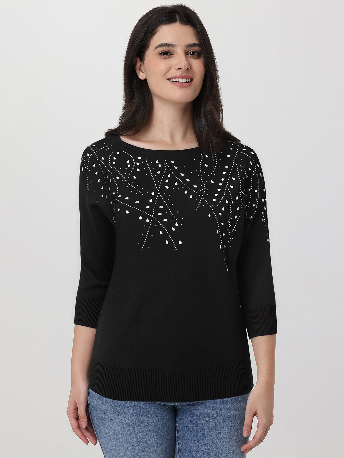 Woman wearing a black sweater with white embellishments on a plain background