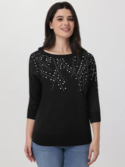 Woman wearing a black sweater with white embellishments on a plain background