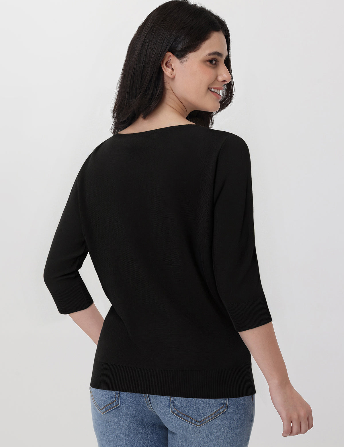 Woman wearing a black top and blue jeans on a white background