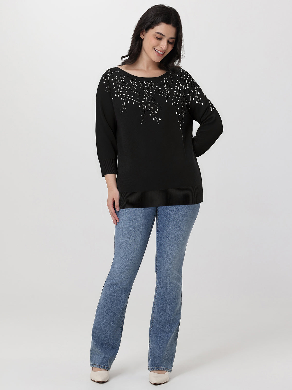 Woman wearing a black embellished top and blue jeans on a white background
