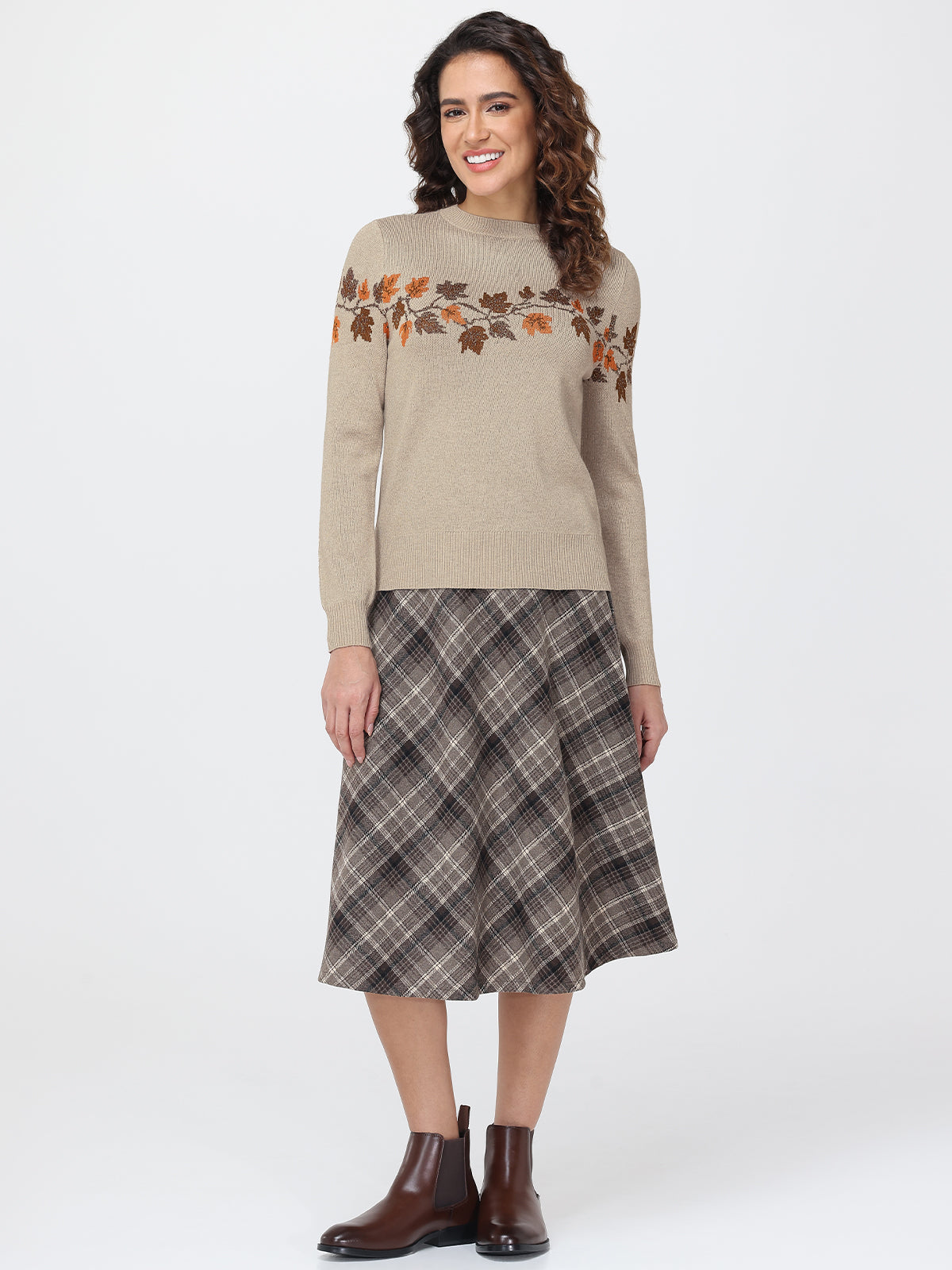 Woman wearing a beige sweater with floral patterns and a plaid skirt on a white background