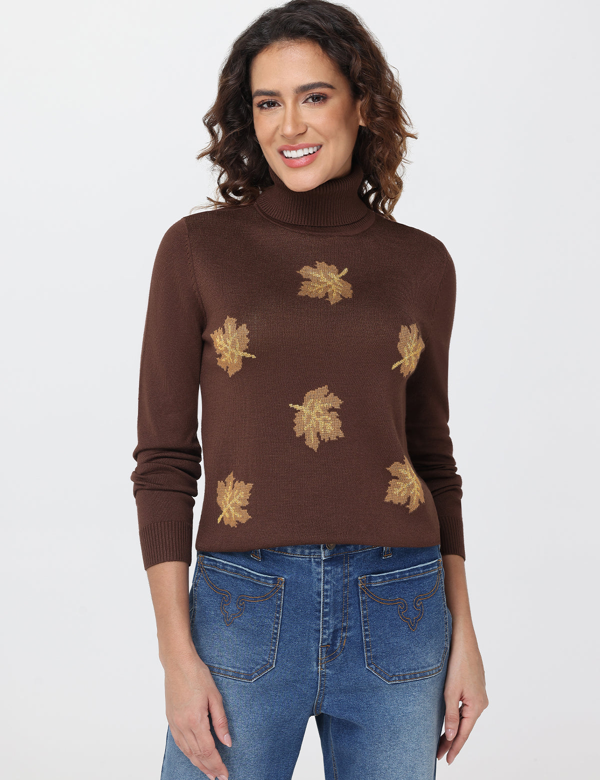Woman wearing a brown turtleneck sweater with leaf patterns and blue jeans on a white background
