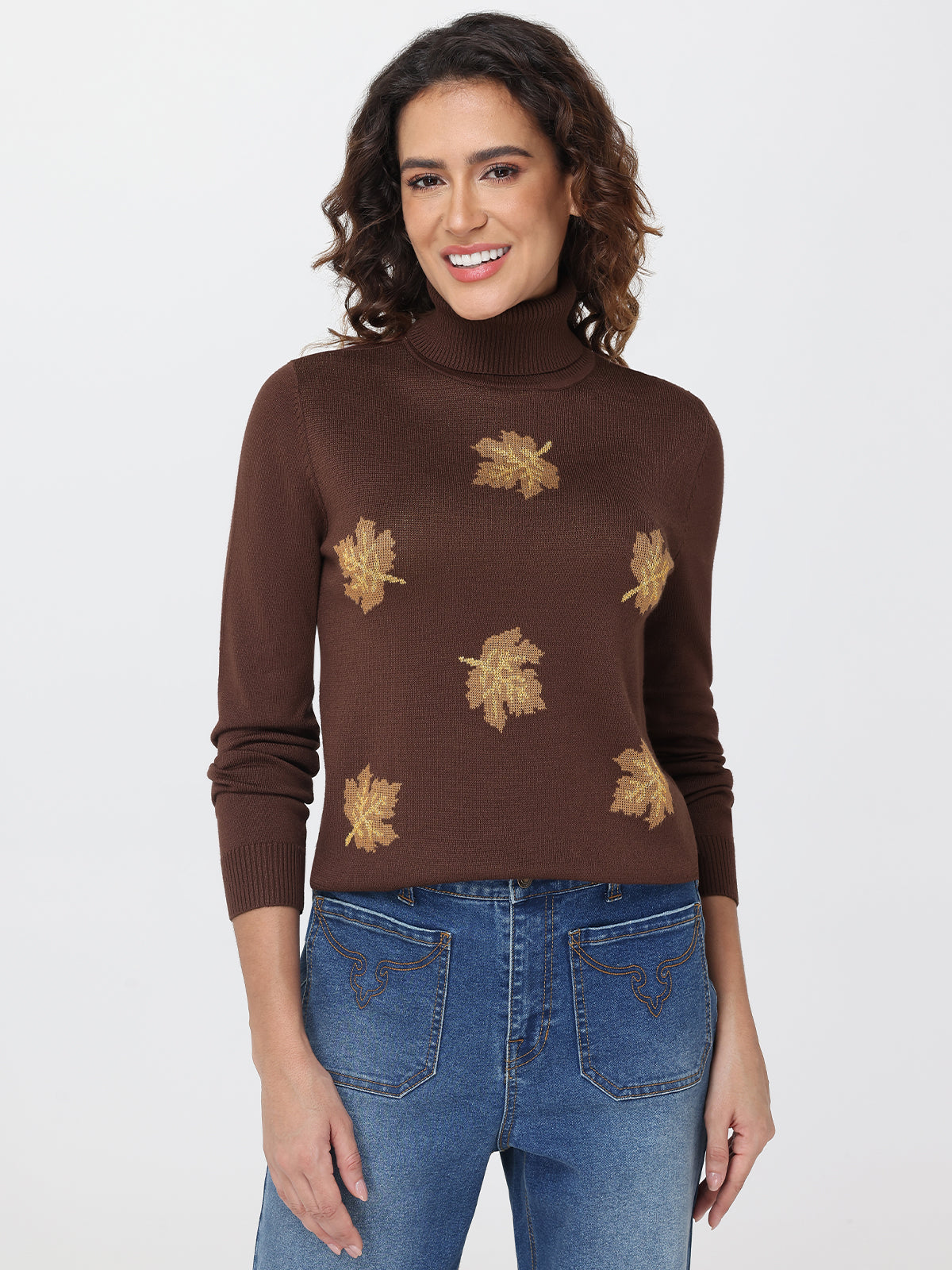Woman wearing a brown turtleneck sweater with leaf patterns and blue jeans on a white background
