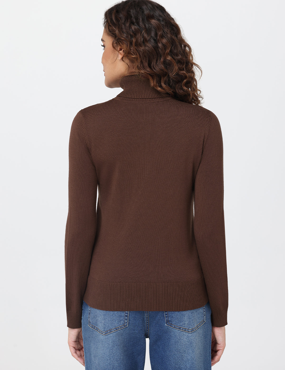 Woman wearing a brown turtleneck sweater and blue jeans on a white background