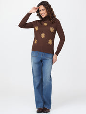 Woman wearing a brown turtleneck sweater with leaf patterns and blue jeans on a white background