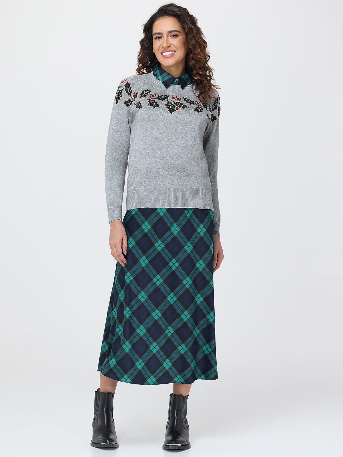 Woman wearing a gray sweater with floral embroidery and a green plaid skirt on a white background