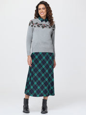 Woman wearing a gray sweater with floral embroidery and a green plaid skirt on a white background