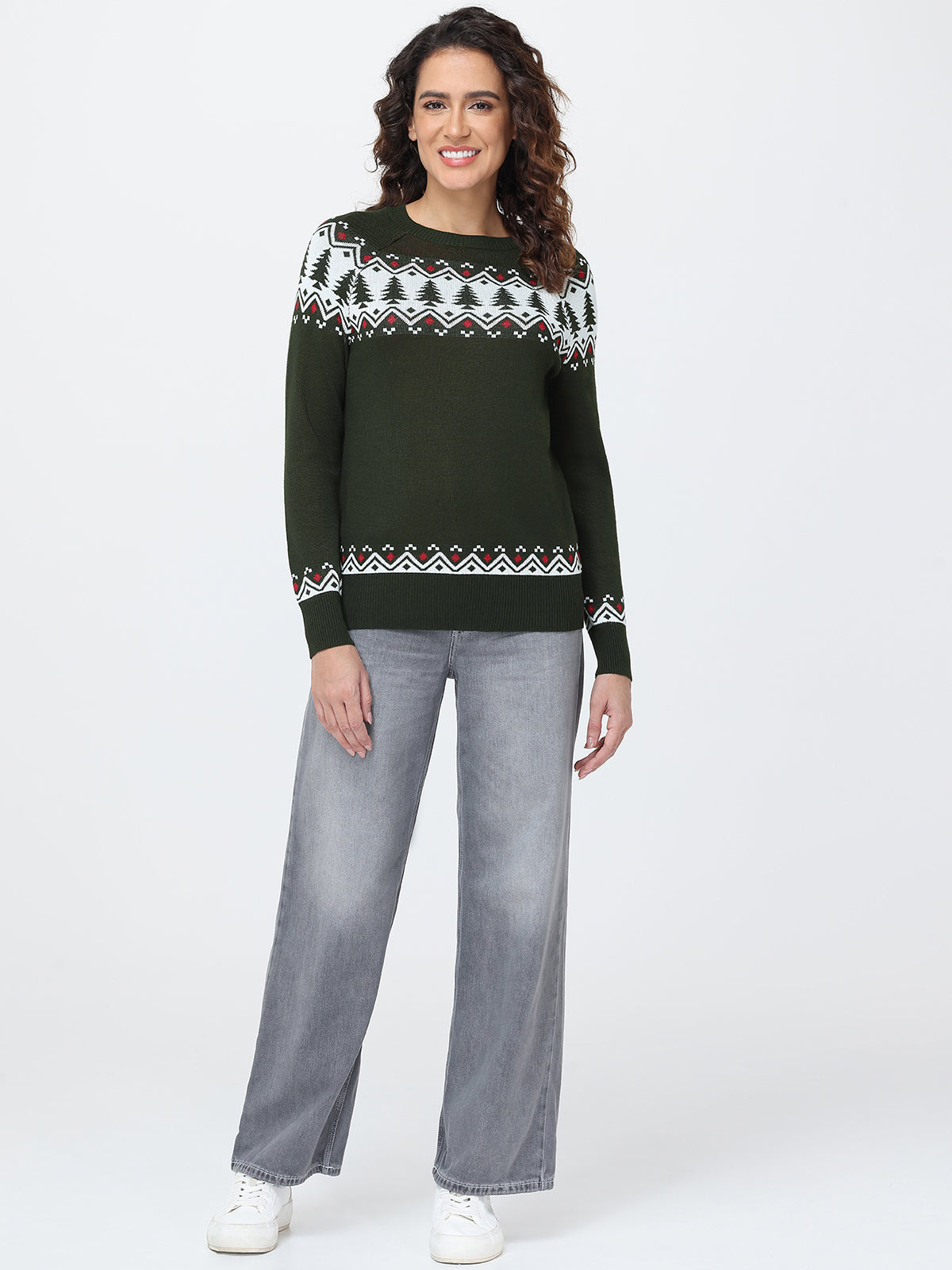 Woman wearing a green sweater with a pattern and gray pants on a white background