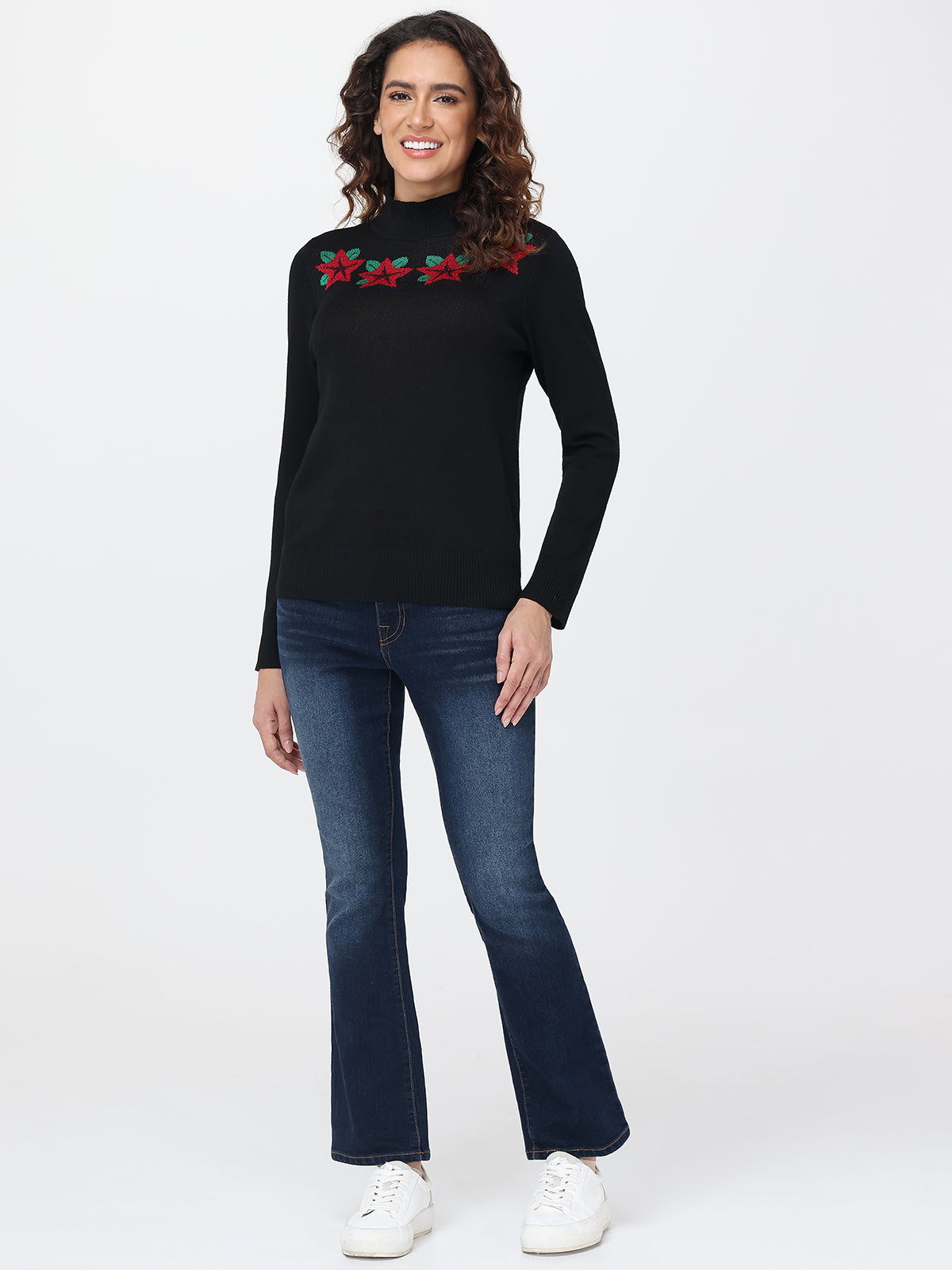 Woman wearing a black sweater with red floral patterns and blue jeans on a white background