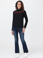 Woman wearing a black sweater with red floral patterns and blue jeans on a white background