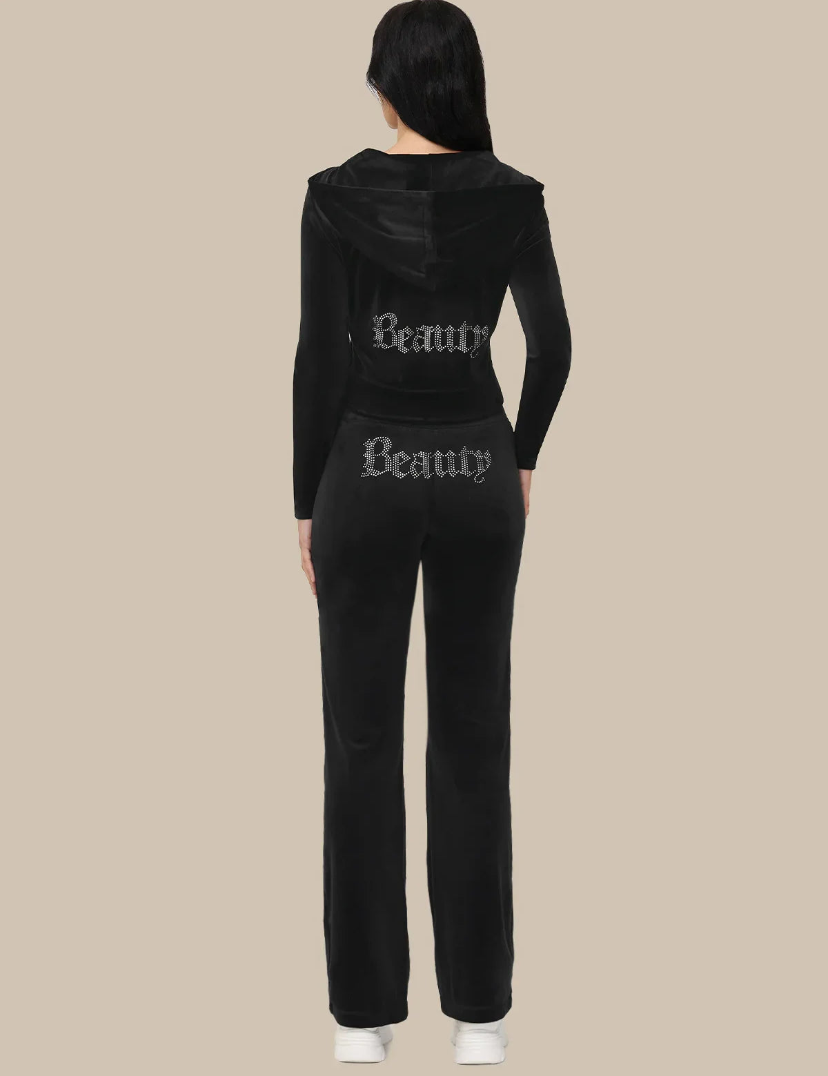 Black tracksuit with 'Beauty' text on the back worn by a person against a beige background