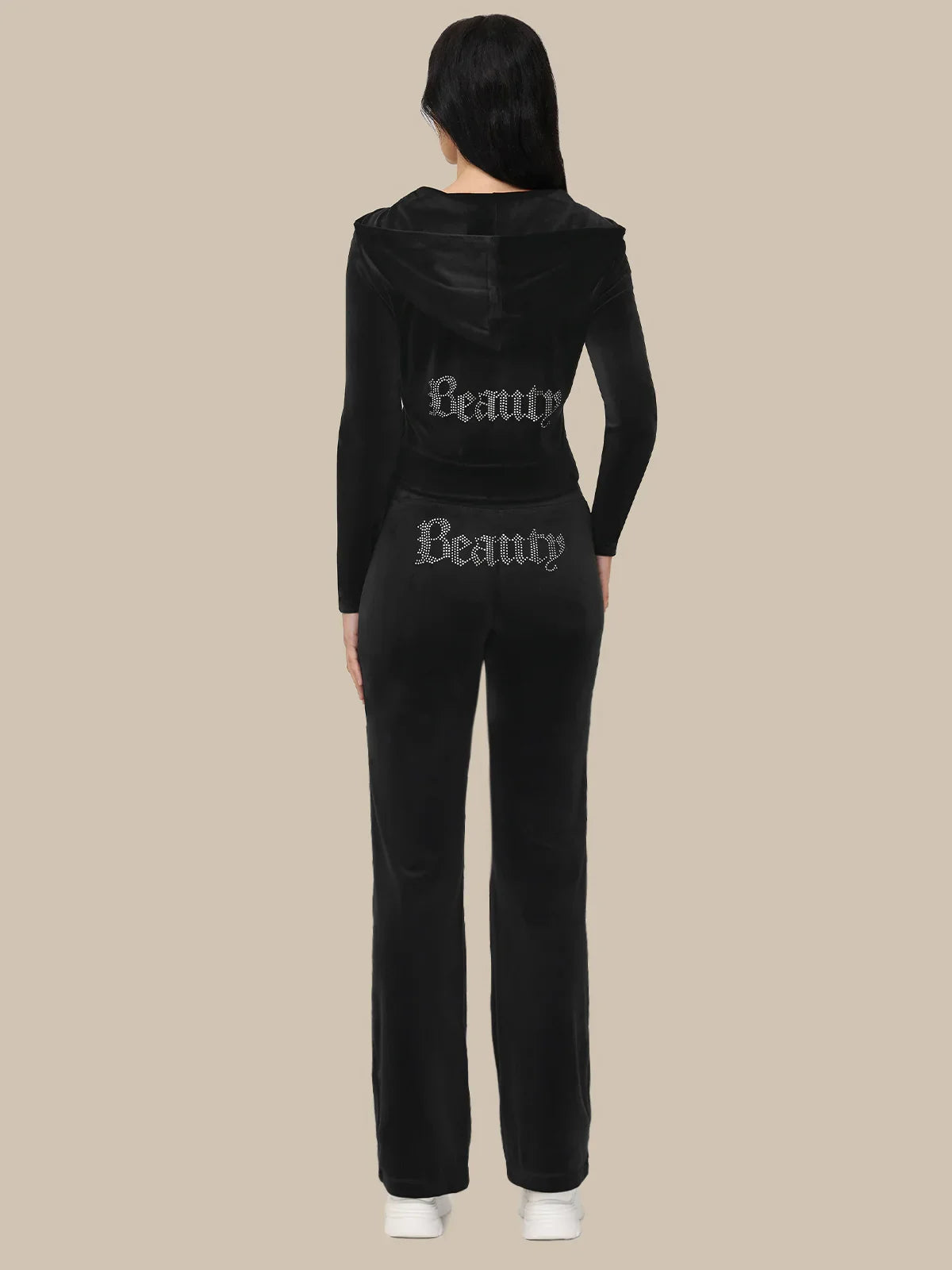 Black tracksuit with 'Beauty' text on the back worn by a person against a beige background