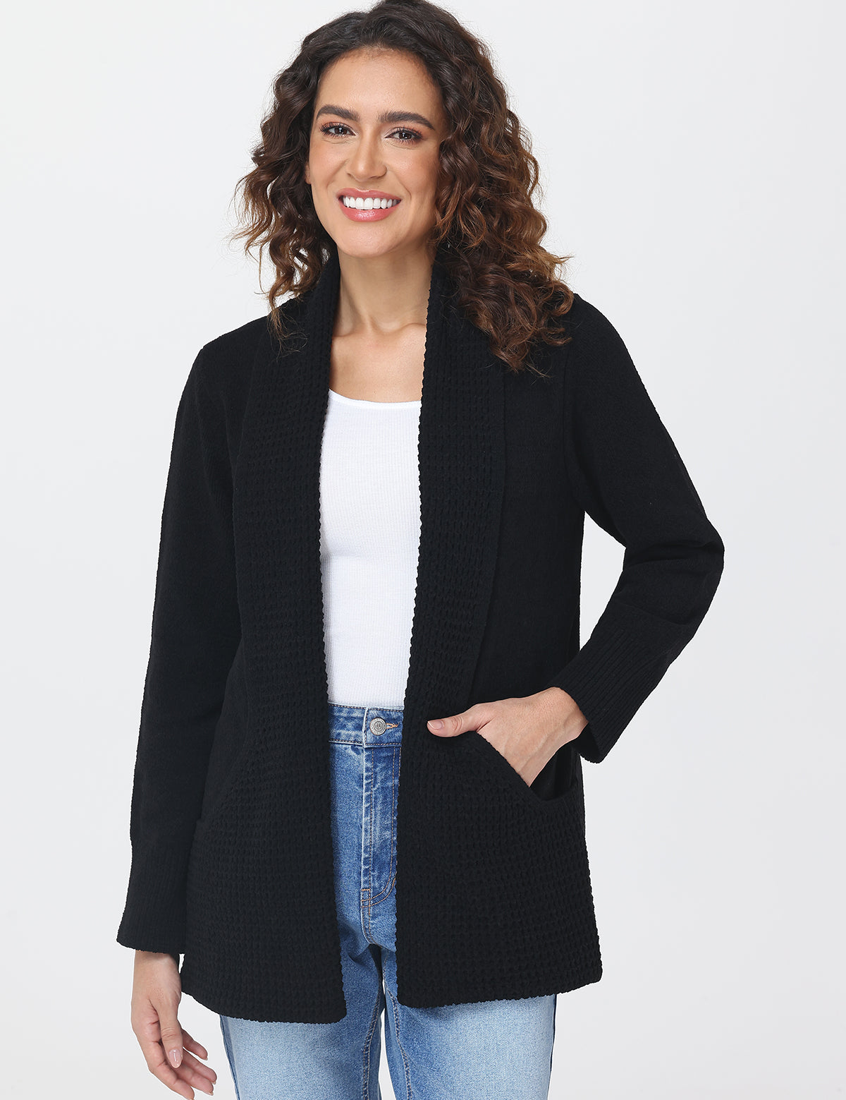 Woman wearing a black cardigan over a white top and blue jeans on a white background