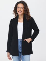 Woman wearing a black cardigan over a white top and blue jeans on a white background