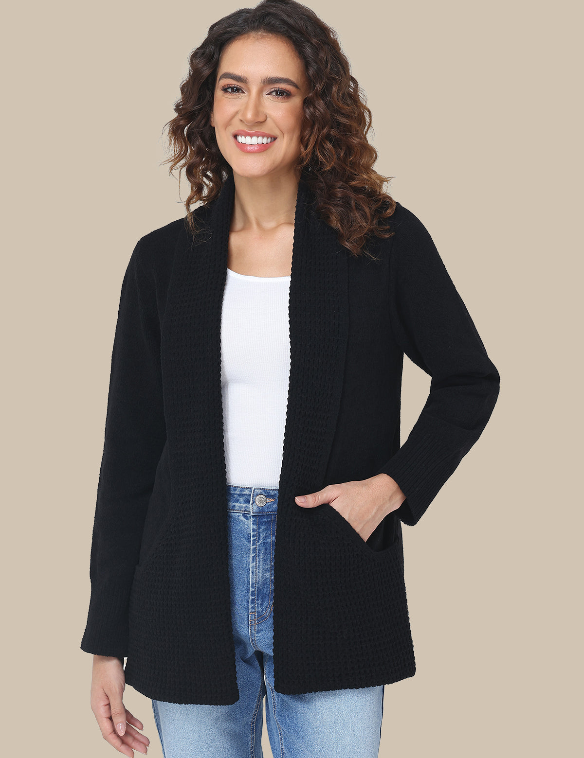 Woman wearing a black cardigan over a white shirt and blue jeans on a beige background