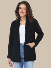 Woman wearing a black cardigan over a white shirt and blue jeans on a beige background