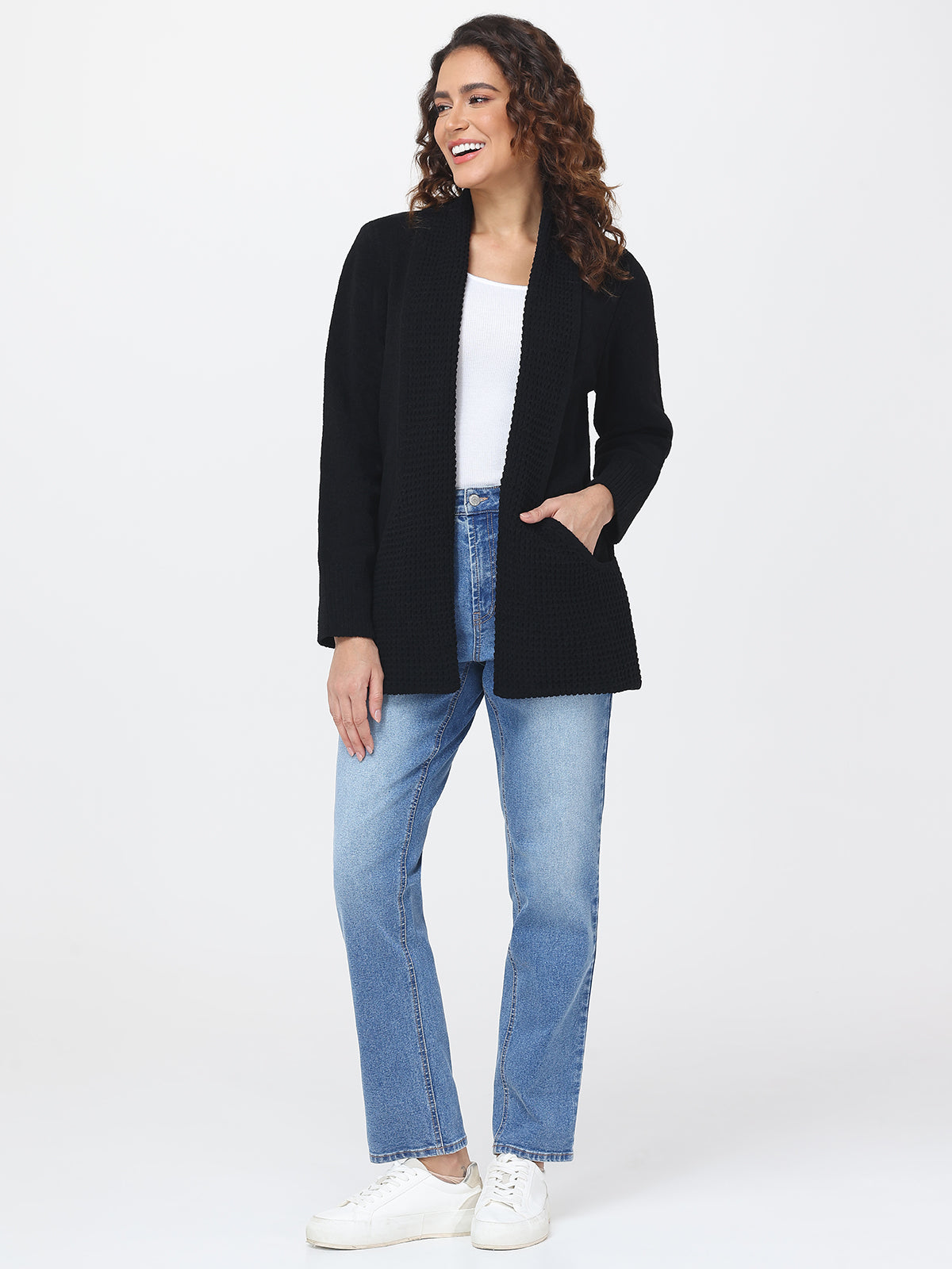 Woman wearing a black cardigan, white top, and blue jeans on a white background