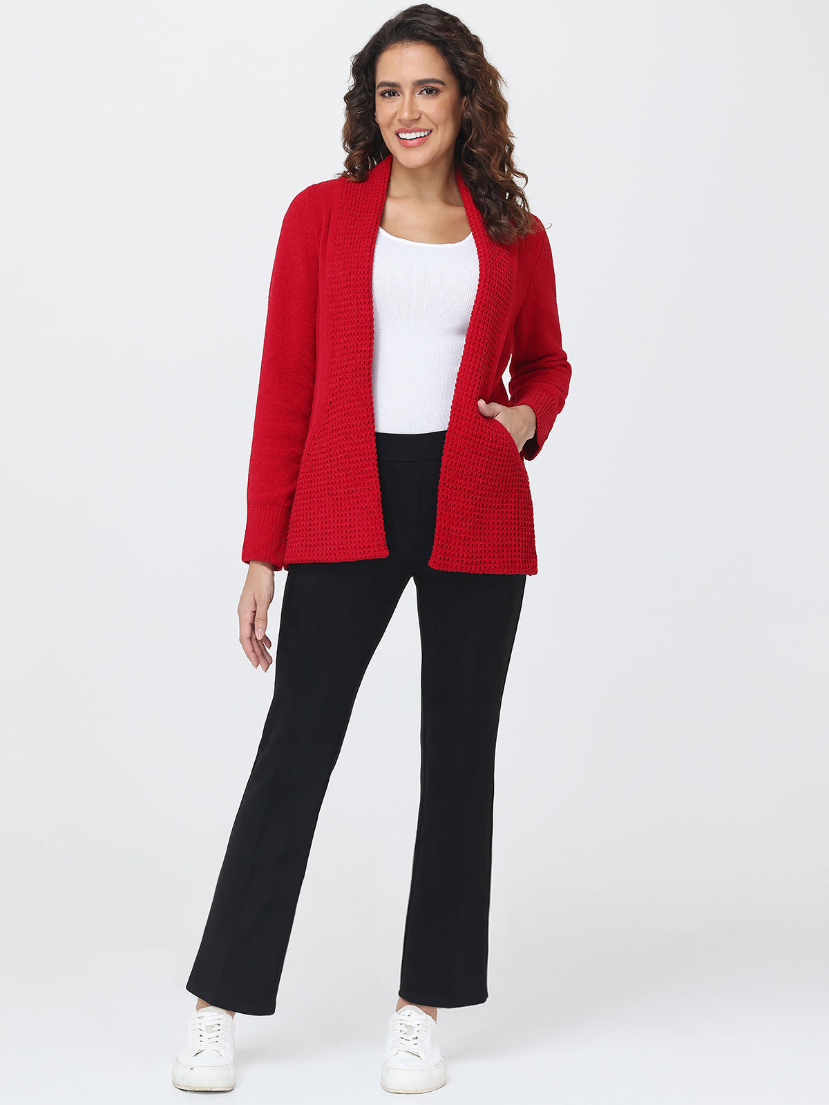 Woman wearing a red cardigan, white top, black pants, and white sneakers on a white background