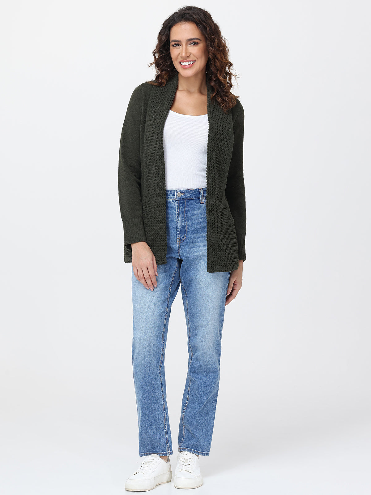 Woman wearing a green cardigan, white top, blue jeans, and white sneakers on a white background