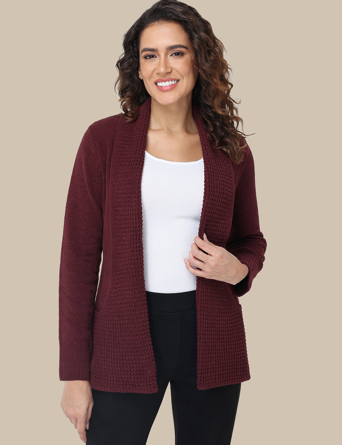 Woman wearing a burgundy cardigan over a white top and black pants on a beige background