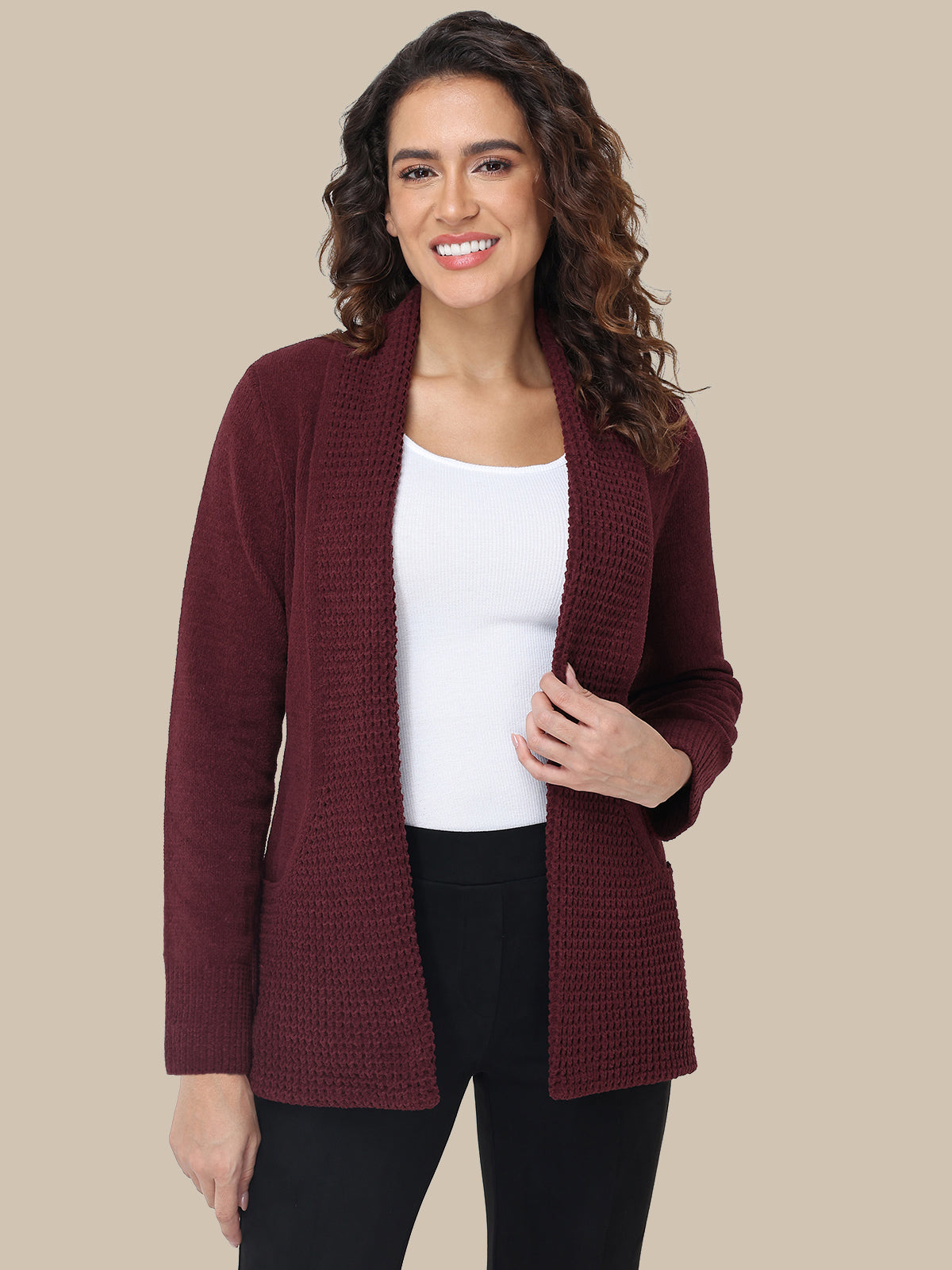 Woman wearing a burgundy cardigan over a white top and black pants on a beige background