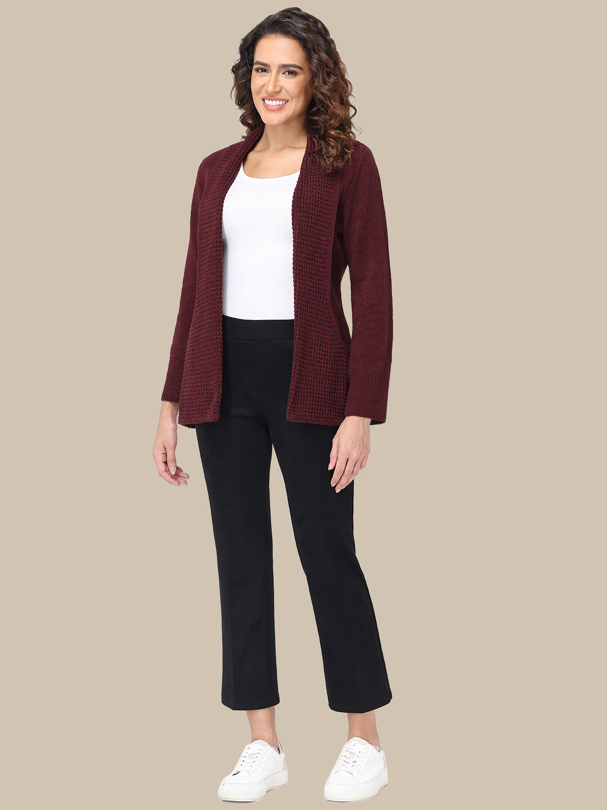 Woman wearing a burgundy cardigan, white top, black pants, and white sneakers on a beige background