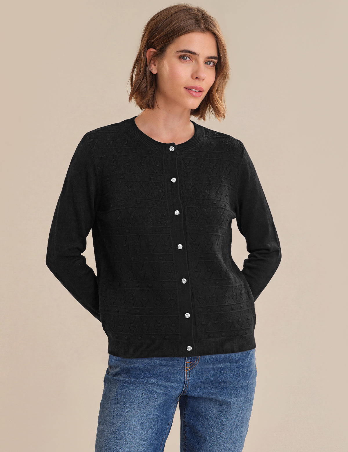 Woman wearing a black cardigan with white buttons on a beige background