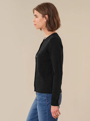 Woman wearing a black cardigan and blue jeans against a beige background
