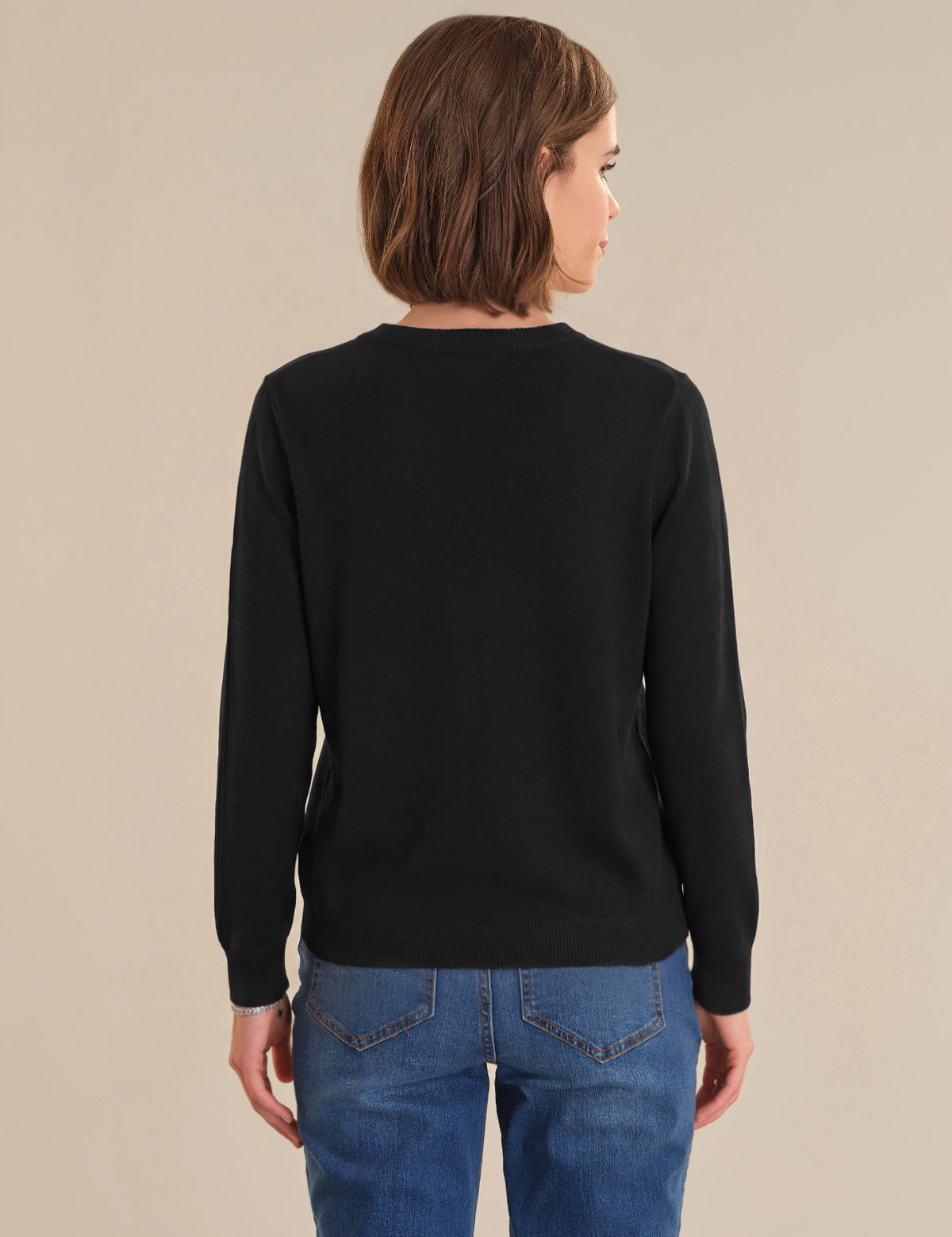 Person wearing a black cardigan and blue jeans on a beige background