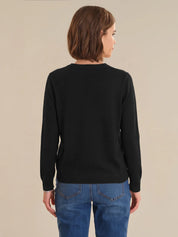 Person wearing a black cardigan and blue jeans on a beige background