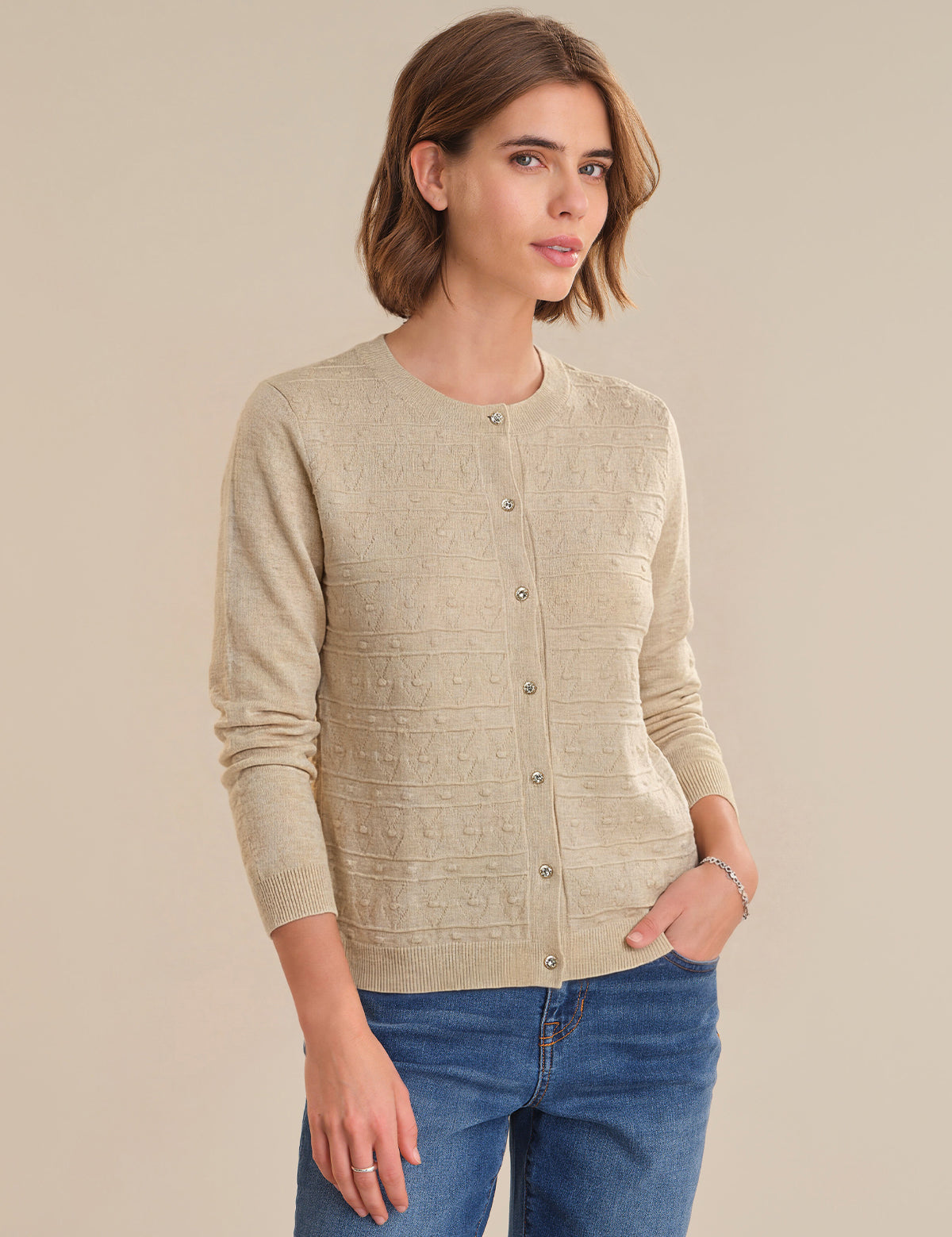 Woman wearing a beige cardigan and blue jeans against a beige background