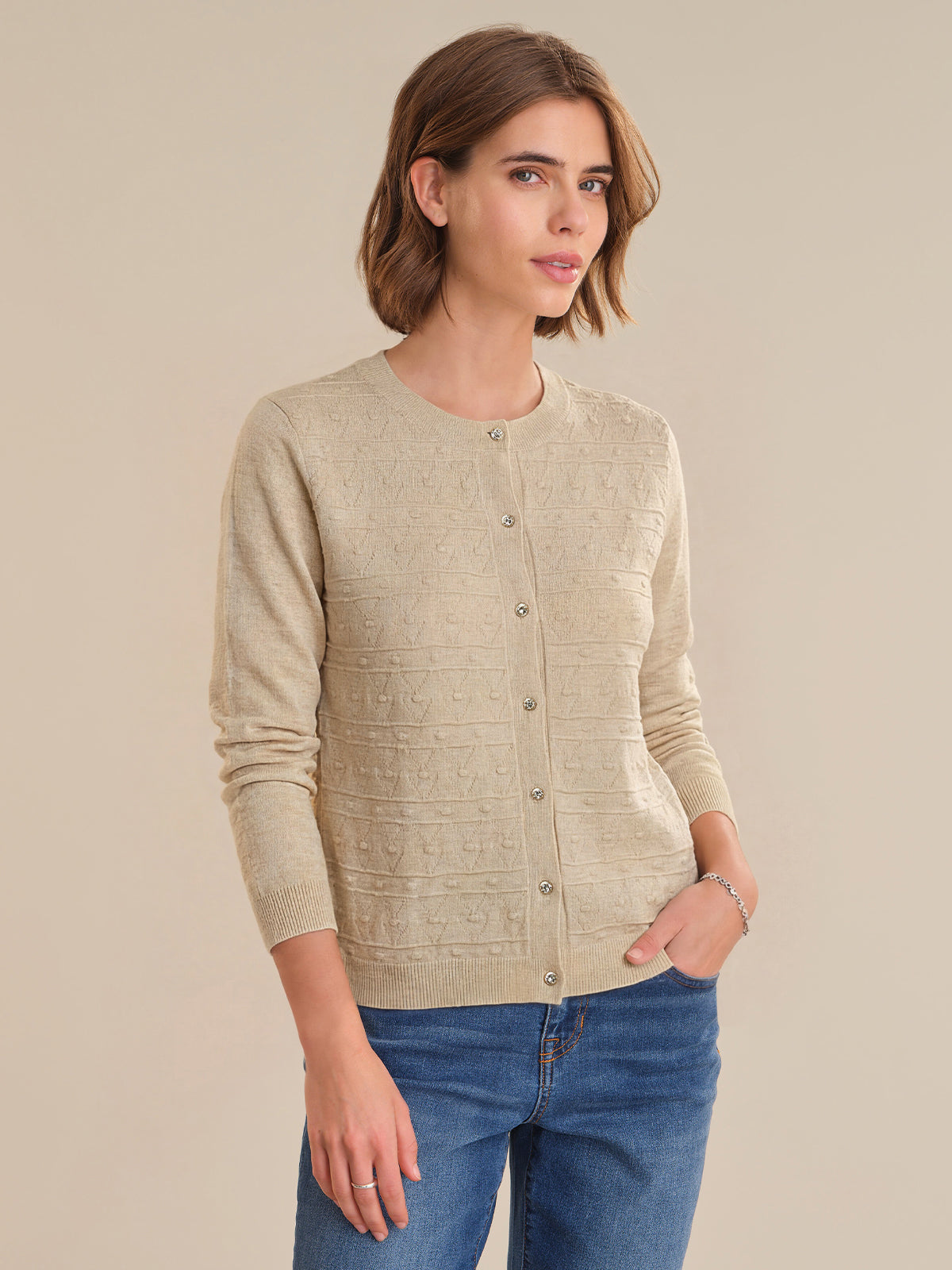 Woman wearing a beige cardigan and blue jeans against a beige background