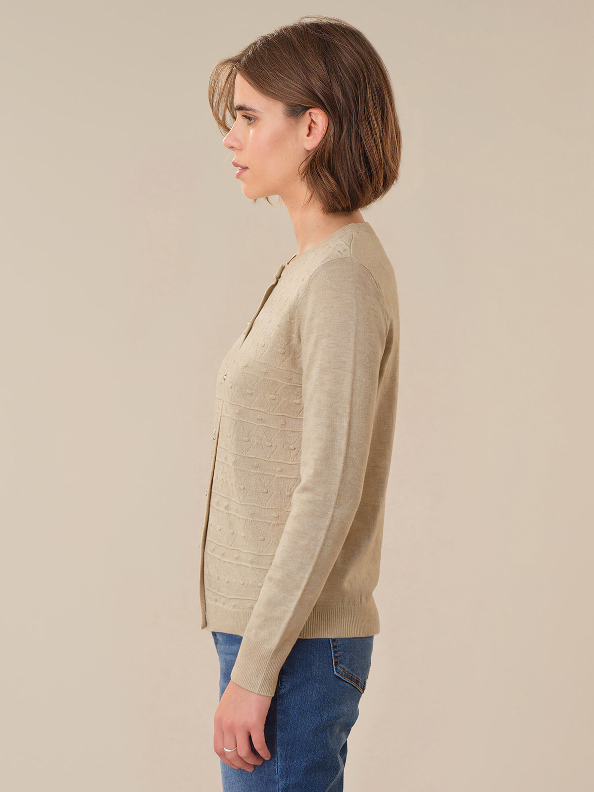 Woman wearing a beige cardigan and blue jeans against a beige background