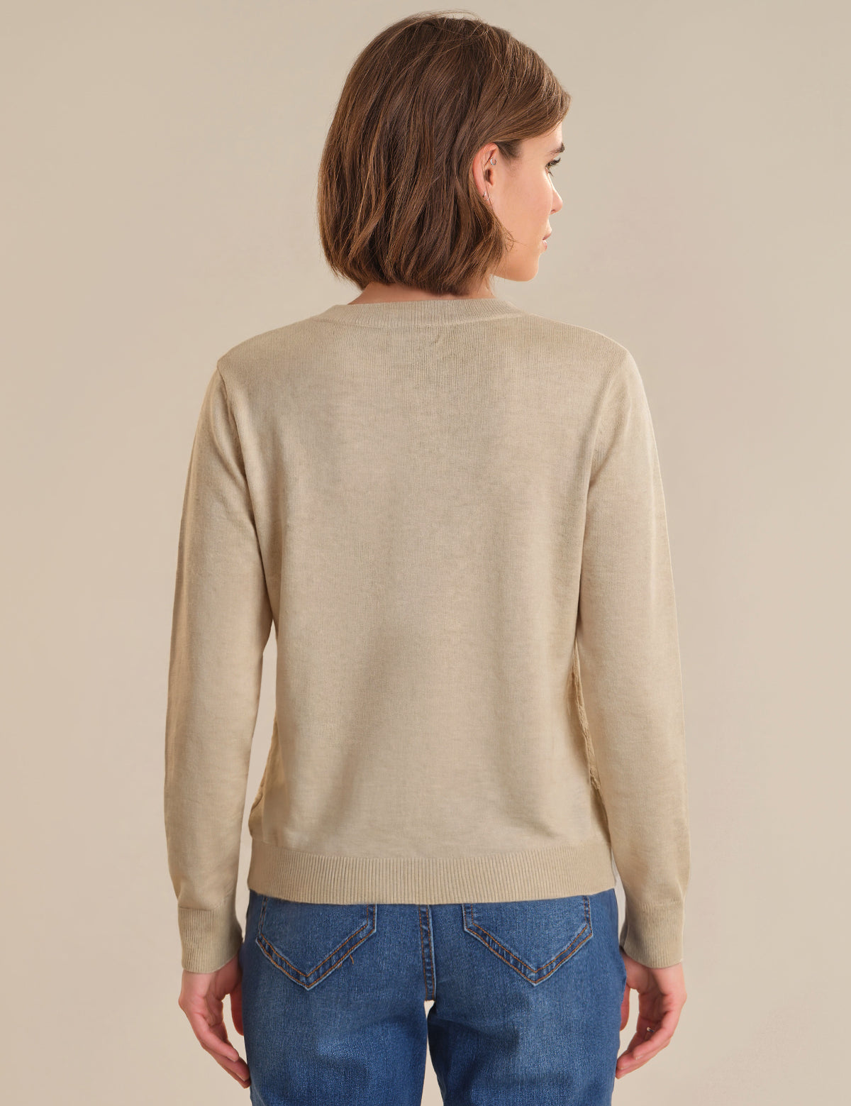 Person wearing a beige sweater and blue jeans against a plain background