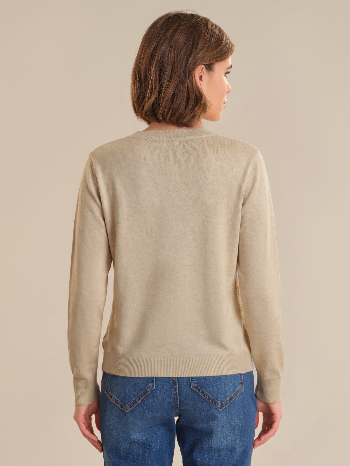 Person wearing a beige sweater and blue jeans against a plain background