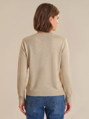 Person wearing a beige sweater and blue jeans against a plain background