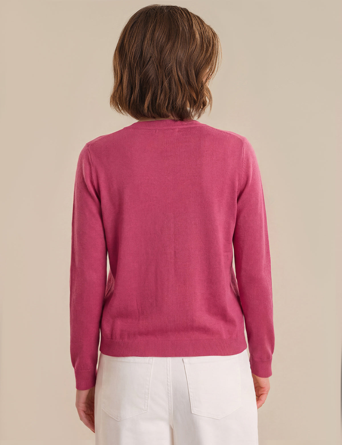 Person wearing a red cardigan and white pants on a beige background