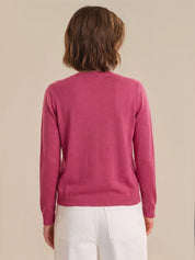 Person wearing a red cardigan and white pants on a beige background