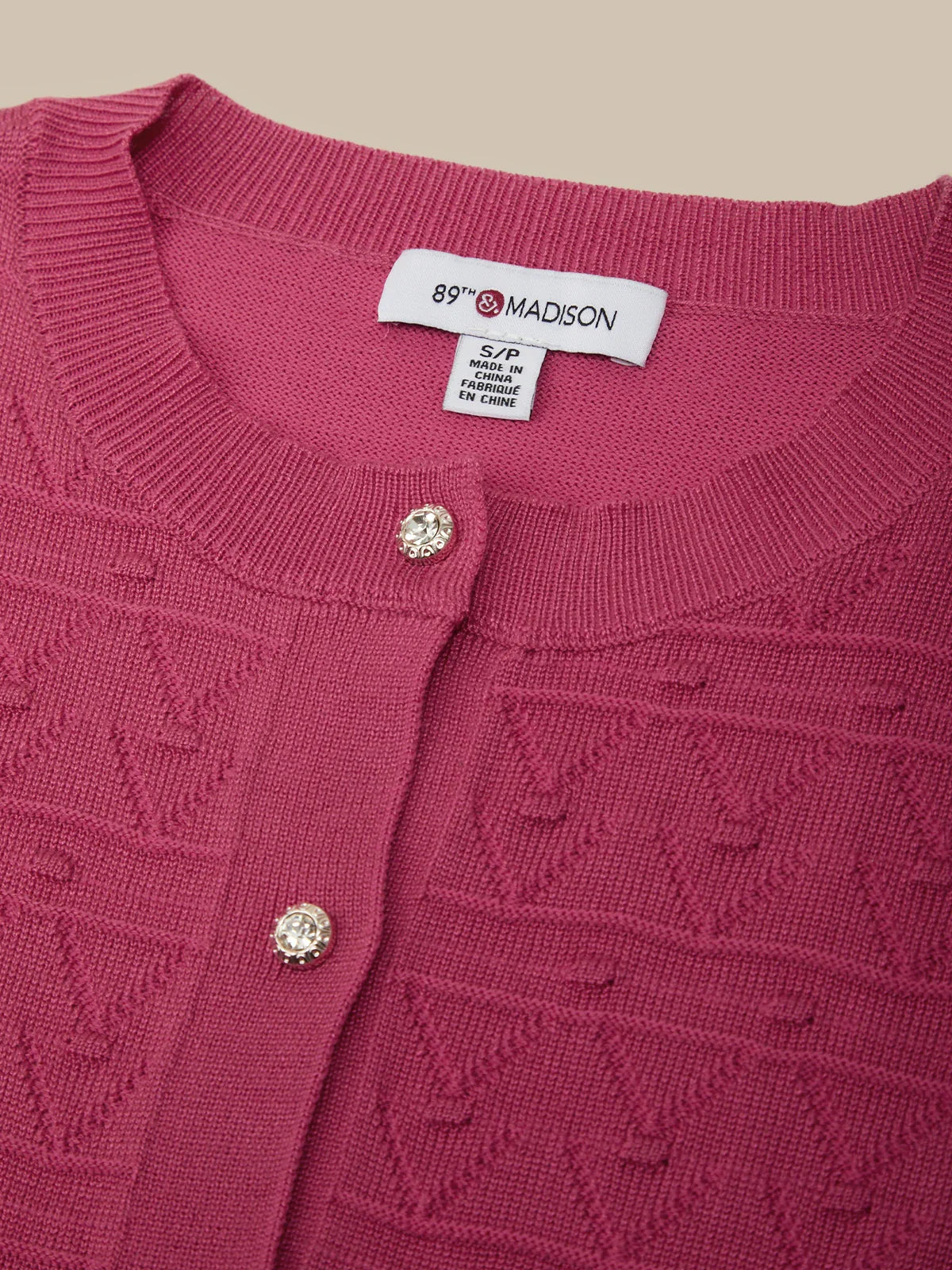 Close-up of a red textured cardigan with '89 & MADISON' label on a beige background