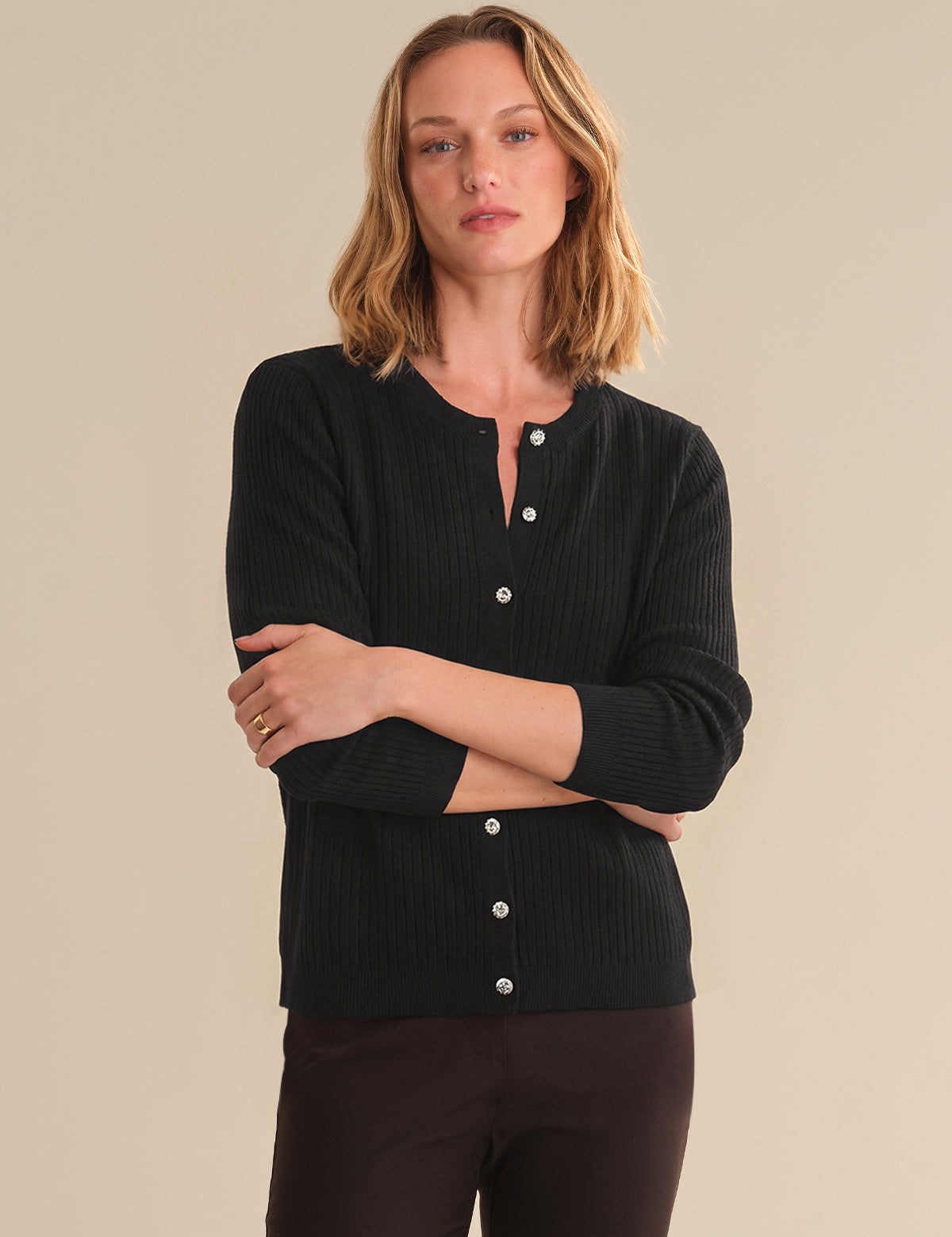 Woman wearing a black ribbed sweater with button details on a beige background